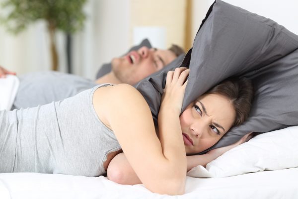 A woman holding a pillow over her ears while her husband snores